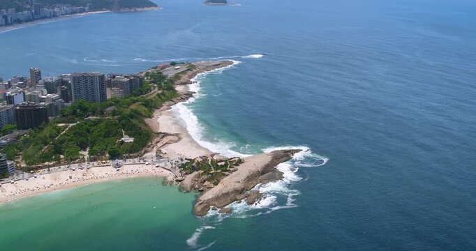 Aerial view of the rocky Arpoador peninsula and sandy beach with turquoise water and urban buildings along the coast in Rio de Janeiro, State of Rio de Janeiro, Brazil.