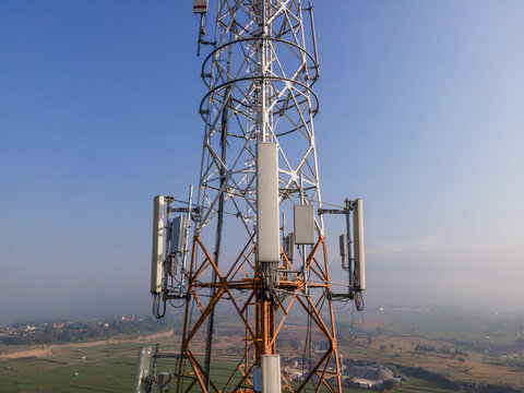 Aerial view of a telecommunications tower with metal lattice structure and antennas overlooking rural fields, Kedungbanteng, Central Java, Indonesia.