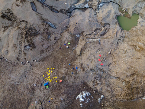 Aerial view of Goro II campsite with colorful tents scattered across the rugged glacial moraine, rocky terrain, and a small glacial pond in Goro II, Gilgit Baltistan, Pakistan.