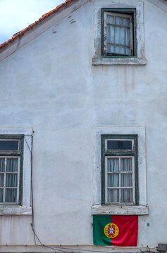 View of a white building facade with traditional windows and a hanging Portuguese flag in Estoril, Lisbon, Portugal.