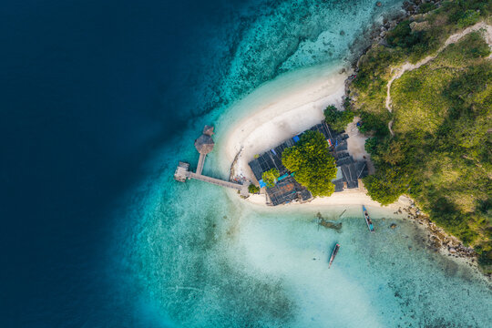Aerial view of Pulau Kelor with its white sand beach, turquoise waters, wooden pier, and lush green hills in Komodo, East Nusa Tenggara, Indonesia.