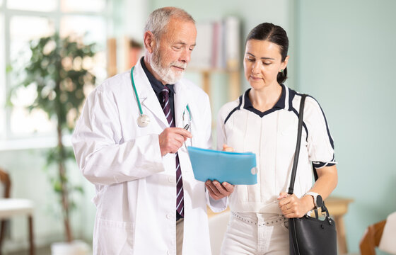 Elderly male doctor sharing positive test results to smiling adult female patient in medical office