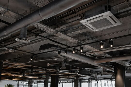  Techo de estilo industrial expuesto con conductos de ventilaci&oacute;n met&aacute;licos, sistema de aire acondicionado y luces modernas en un espacio comercial