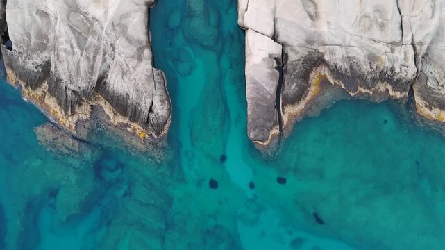 Drone view over the rocky shore of Mandrakia on Milos, Greece, showing crystal clear turquoise Aegean water beside rugged land as the camera drifts sideways revealing the unique coastal landscape.