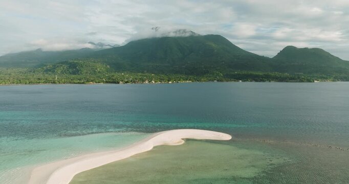 Aerial view of White Island sandbar surrounded by turquoise waters with lush green mountains in the background in Mambajao, Camiguin, Philippines.