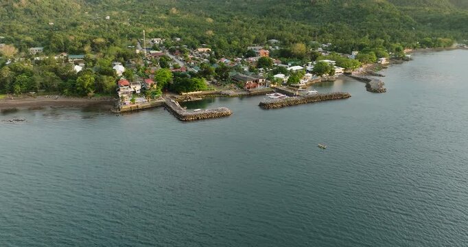 Aerial view of the coastal town of Mambajao with its stone piers, lush green hills, and calm sea waters in Mambajao, Camiguin, Philippines.