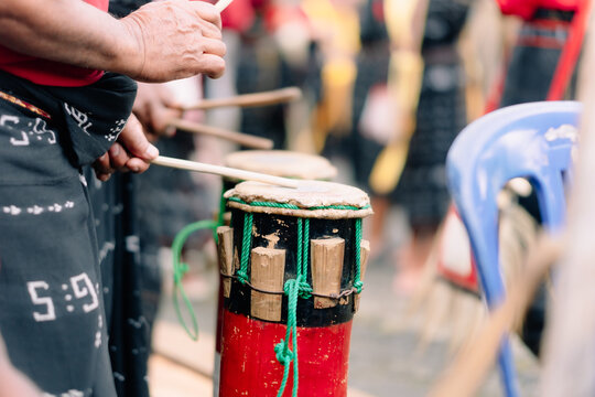 Bajawa, Indonesia - 09 July 2026: View of a person playing a traditional drum with wooden sticks while wearing a patterned sarong during a cultural ceremony.