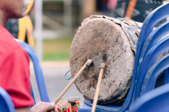 Bajawa, Nusa Tenggara Timur, Indonesia - 09 July 2026: View of a person playing a traditional drum with wooden sticks, accompanied by blue plastic chairs in the background.