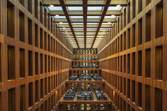 View of the Jacob-und-Wilhelm-Grimm-Zentrum library interior with symmetrical wooden shelves, study desks, and natural light from the skylight in Berlin, Berlin, Germany.
