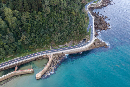 Aerial view of the primer tunel de Zarautz along the coastal road with rocky cliffs, lush green hills, and the blue sea in Zarautz, Basque Country, Spain.