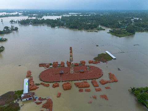 Aerial view of a flooded brick kiln with a tall chimney and stacks of red bricks surrounded by floodwater in Banshkhali Upazila, Chittagong Division, Bangladesh.