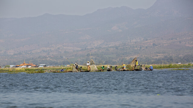 View of Inle Lake with traditional fishermen in wooden boats using conical nets under a clear sky in Taunggyi, Shan, Myanmar.