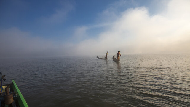 View of Inle Lake with traditional fishermen in wooden boats on the water during a misty morning in Taunggyi, Shan, Myanmar.