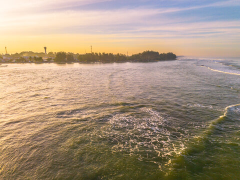 Aerial view of Pantai Panjang Bengkulu with gentle waves rolling onto the sandy shore under a warm golden sunset sky in Kecamatan Ratu Agung, Bengkulu, Indonesia.