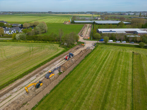 Aerial view of construction work with excavators digging a trench through green agricultural fields in the Netherlands.
