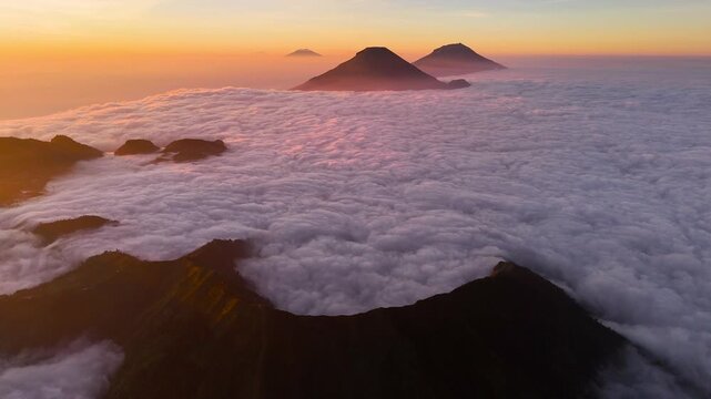 Aerial view of Gunung Bismo rising above a thick sea of clouds during golden hour in Kecamatan Kejajar, Jawa Tengah, Indonesia.