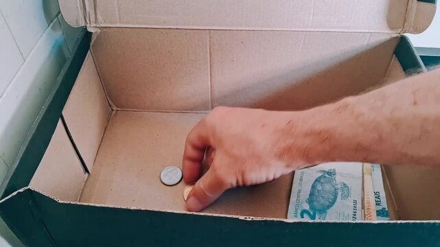 Hand collecting Brazilian coins into cardboard box for motion video footage