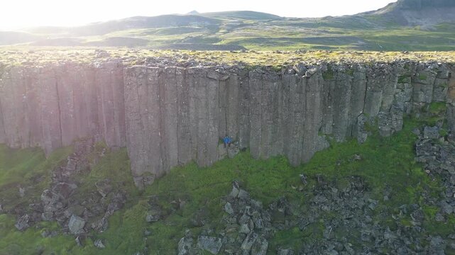 Aerial view of a person in a blue jacket sitting at the base of the basalt columns of Gerduberg Cliffs in Raudhamelur, Eyja- og Miklaholtshr, Iceland.