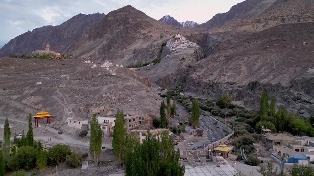 Aerial view of Diskit Monastery nestled in the rugged mountains of the Himalayas with green trees and village houses below in Diskit, Ladakh, India.