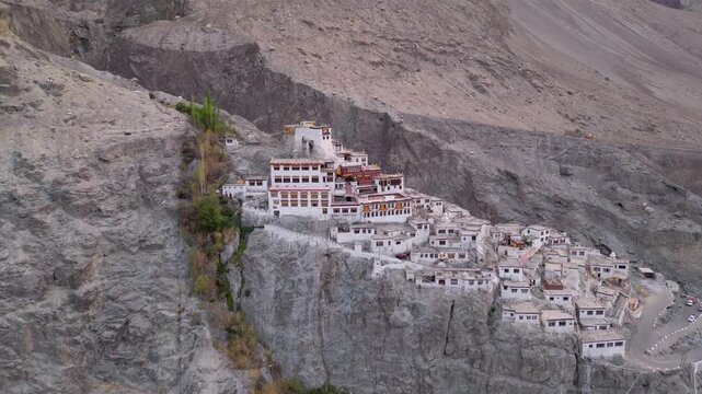 Aerial view of Diskit Monastery built into the rocky cliffside with traditional white buildings and a winding road below in Diskit, Ladakh, INDIA.