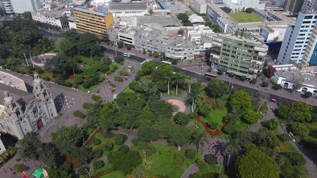 Aerial view of the historic Parroquia Virgen Milagrosa and the lush green Parque Kennedy surrounded by urban streets and buildings in Miraflores, Lima Province, Peru.