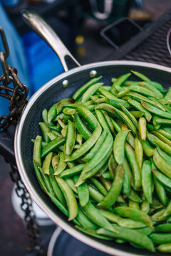 A pan full of green beans cooking over a fire on an outdoor cooker