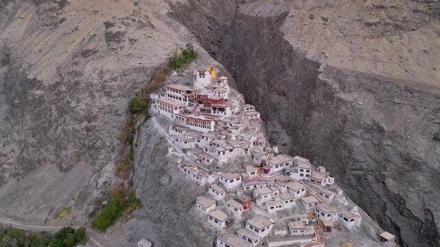 Aerial view of Diskit Monastery with its white buildings perched on a rocky cliff in the arid mountain landscape of Diskit, Ladakh, INDIA.