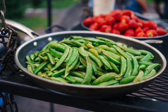 Beans cooking in a pan with a pan of tomatoes cooking in the background