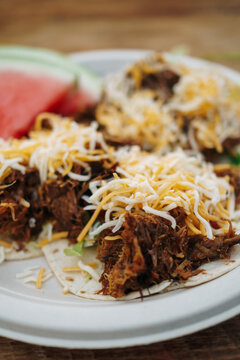 Pulled pork tacos with shredded cheese on top with watermelon in the background at a barbecue