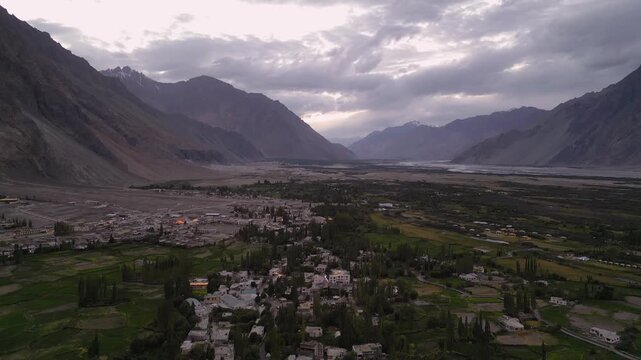Aerial view of Diskit Monastery nestled in the mountains of the Nubra Valley, with lush green fields and the village of Diskit below under a cloudy sky in Diskit, Ladakh, India.