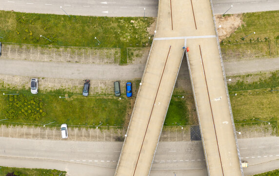 Aerial view of the Y-shaped pedestrian bridge near Ergo Arena with parked cars on the surrounding asphalt and green grass areas in Gdansk, Wojewodztwo pomorskie, Poland.