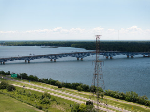 Aerial view of the North Grand Island Bridge spanning the Niagara River with a power transmission tower in the foreground, green banks, and blue sky in Niagara Falls, New York, United States.