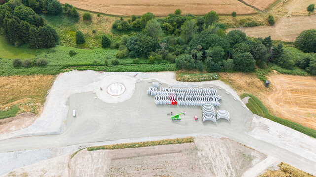 Aerial view of a wind turbine construction site with a circular foundation and stacked concrete segments in a rural landscape in Trier-Saarburg, Rhineland-Palatinate, Germany.