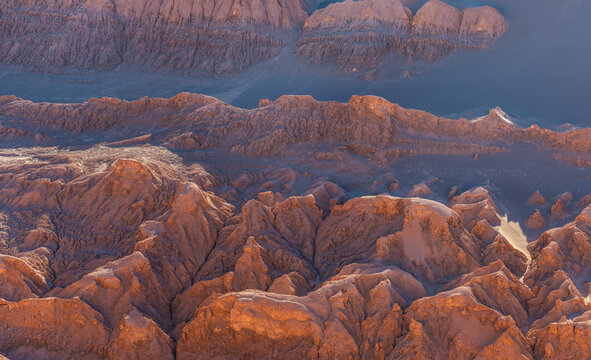 Aerial view of the rugged Valley of the Moon, featuring dramatic rock formations and deep canyons under soft golden light in San Pedro de Atacama, Antofagasta, Chile.