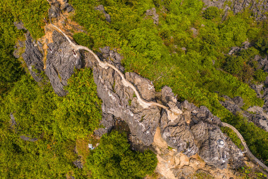 Aerial view of the stone path leading to the Hang Mua Big Pagoda, winding over rugged limestone karst mountains surrounded by lush green vegetation in Nam Hoa Lu, Ninh Binh, Vietnam.