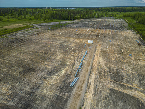 Aerial view of a solar farm construction site with rows of metal mounting structures, a dirt road, and surrounding forest in Riga, Latvia.