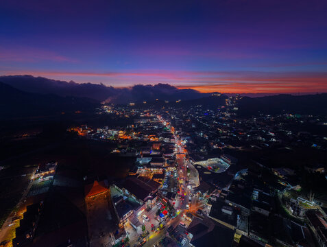 Aerial view of the town of Dieng illuminated at twilight with vibrant sunset colors over the mountainous landscape of Kejajar, Central Java, Indonesia.
