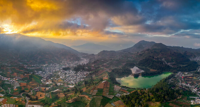 Aerial view of Telaga Warna lake surrounded by lush terraced agricultural fields and the town of Kejajar, Central Java, Indonesia.