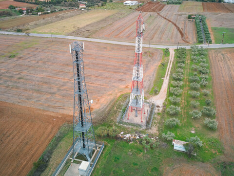 Aerial view of two communication towers standing in a rural landscape with cultivated fields and rows of olive trees in Greece.
