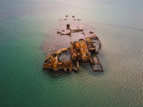 Aerial view of the rusted remains of a shipwreck partially submerged in the clear turquoise waters off the coast of Greece.