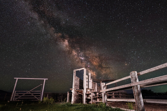 View of the old wooden cattle chute under the starry night sky with the Milky Way galaxy visible above the rural landscape in Picabo, Idaho, United States.