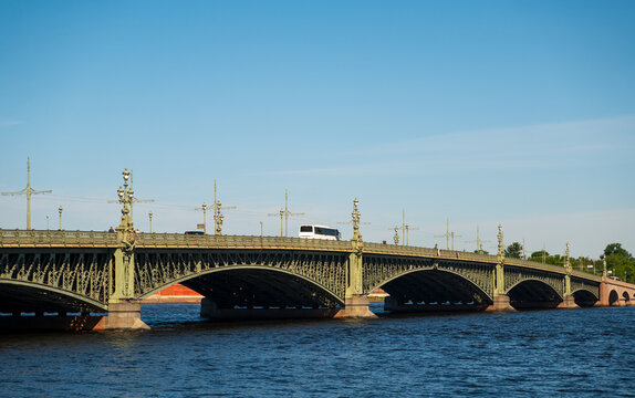 View of the ornate metal arches and decorative lampposts of the historic Trinity Bridge spanning the Neva River in Saint Petersburg, Russia.