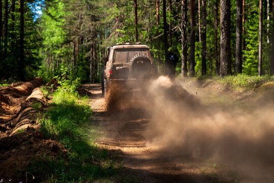 View of an off-road vehicle driving on a dirt path through a forest near Lake Ladoga, kicking up a cloud of dust in Sortavala, Respublika Kareliya, Russia.