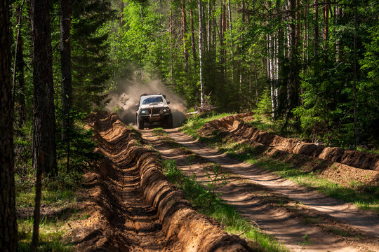 View of an off-road vehicle driving on a dirt track through a dense forest near Lake Ladoga, kicking up dust in the sunlight in Sortavala, Respublika Kareliya, Russia.