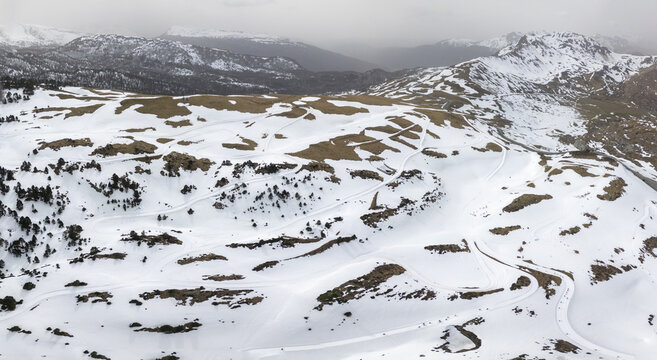 Aerial view of cross-country skiing tracks winding through a snow-covered mountain landscape with sparse trees and distant peaks in Isaba, Navarre, Spain.