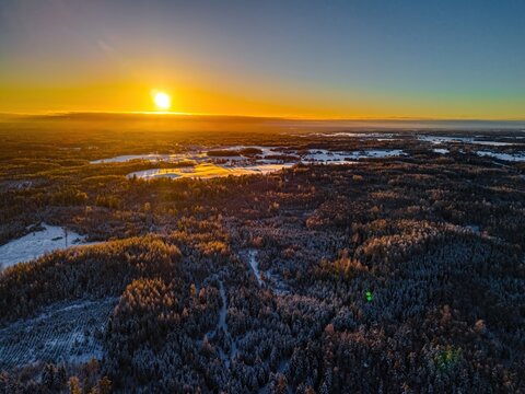 Aerial view of a snow-covered forest landscape illuminated by the warm golden light of a winter sunset in Riga, Latvia.