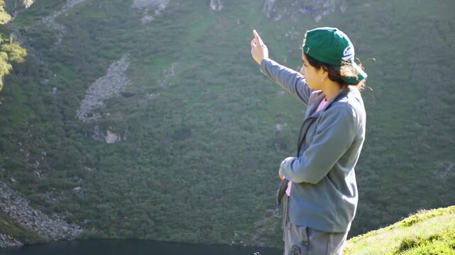 Young woman hiking points at a mountain lake in the green alpine highlands
