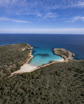 Aerial view of Cala Varques with turquoise waters, rocky cliffs, and Mediterranean scrubland in Mallorca, Spain.