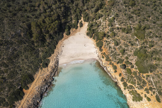 Aerial view of Cala Varques with its white sand beach, turquoise waters, and surrounding rocky cliffs and pine forests in Mallorca, Spain.