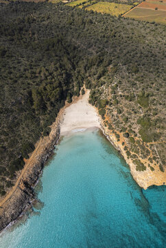 Aerial view of Cala Varques featuring a secluded sandy beach with turquoise water surrounded by rocky cliffs and Mediterranean forest in Mallorca, Spain.